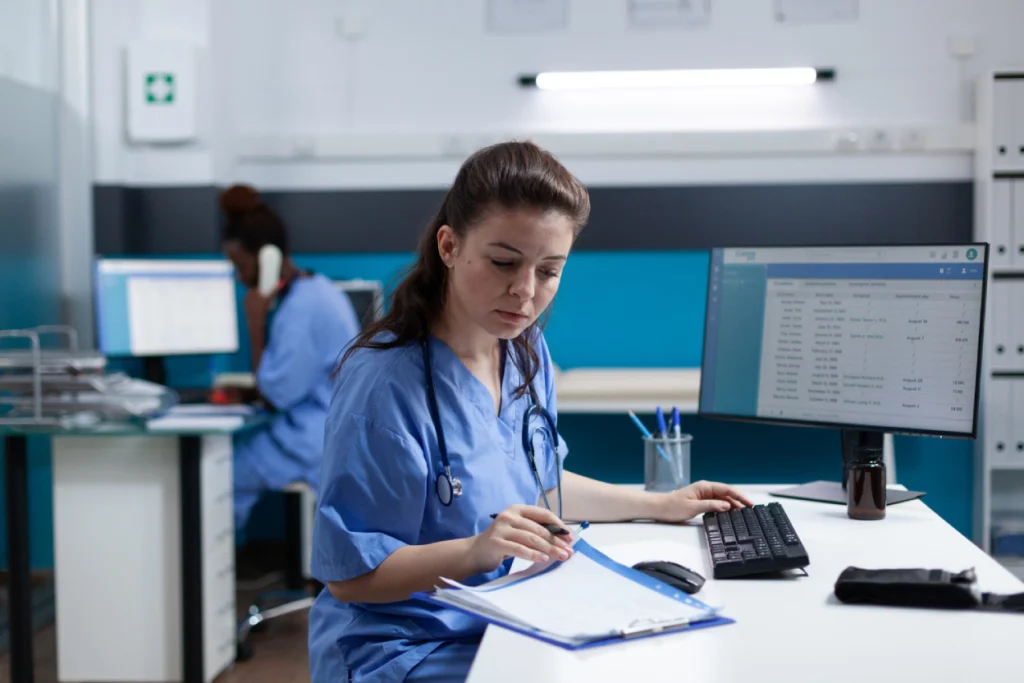 Medical Coding Explained: Types, Careers, Tools & Future Trends 9 Medical coder in scrubs reviewing patient records at a clinic workstation