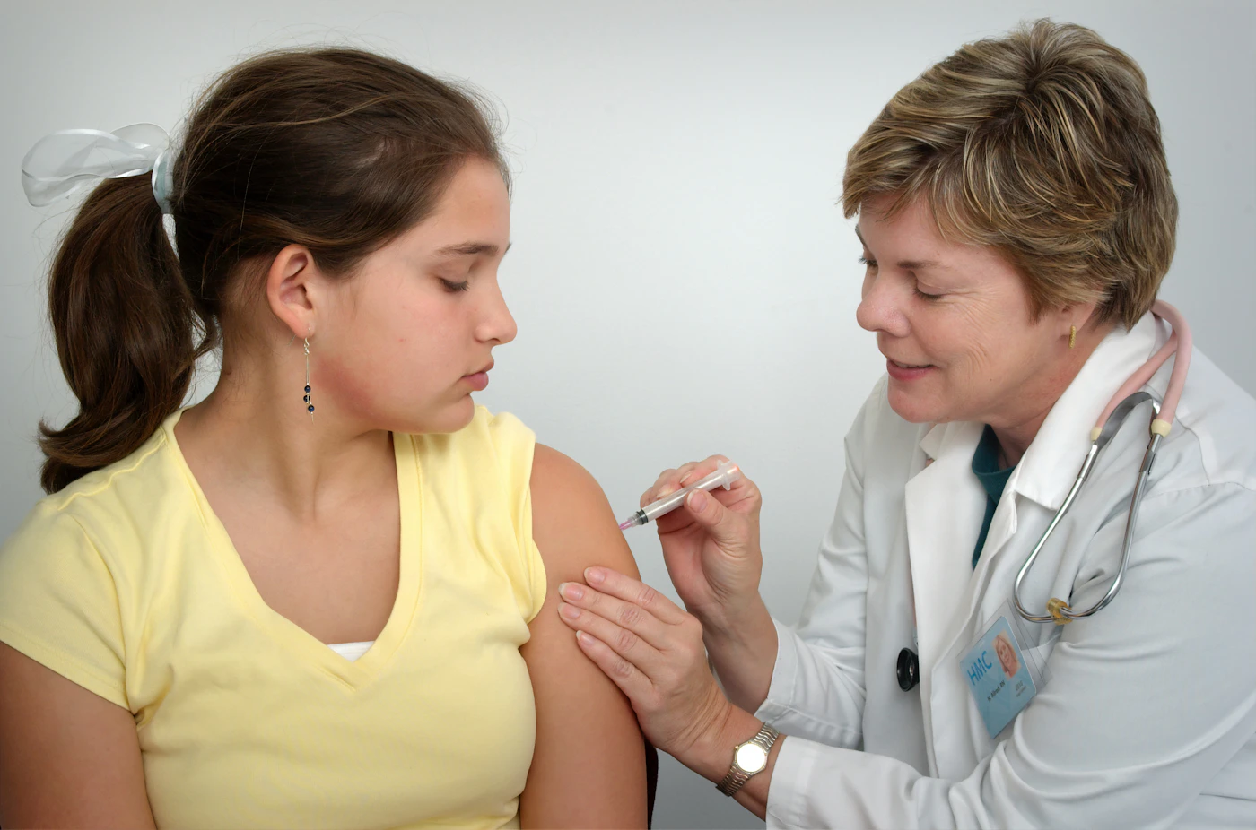 Doctor giving a teenage girl an injection in the upper arm