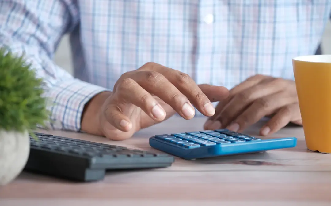 Hands working a calculator on a desk next to a keyboard