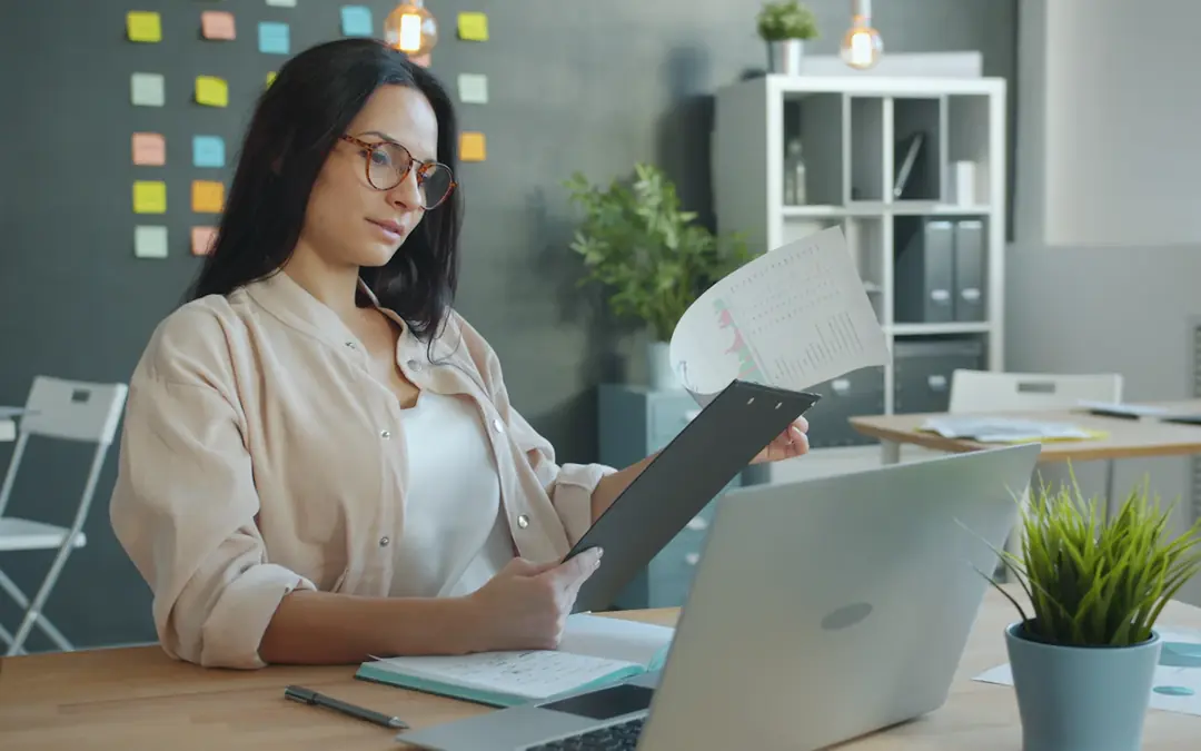 Woman reviewing a document from her clipboard at an office desk