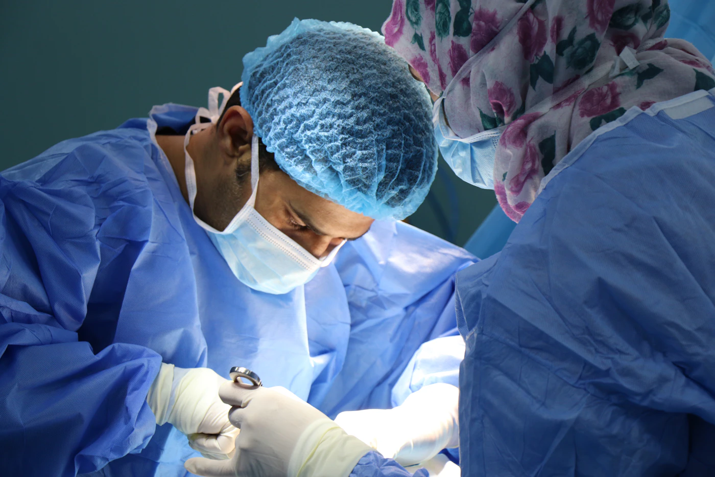 Surgeon in blue scrubs and a mask operating under bright lights