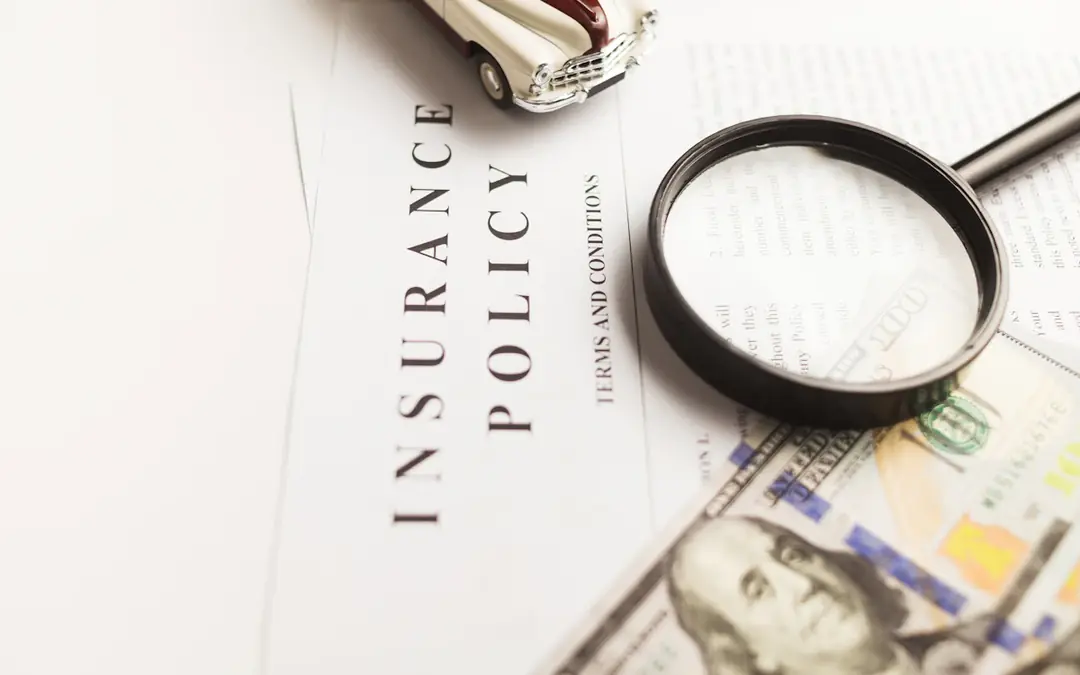 Magnifying glass over an insurance policy and dollar bills