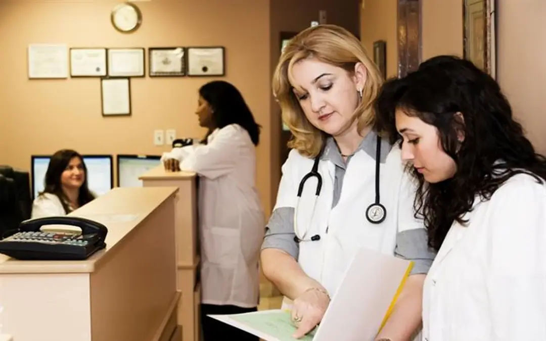 Two physicians reviewing paperwork at a clinic front desk with framed certificates on the wall