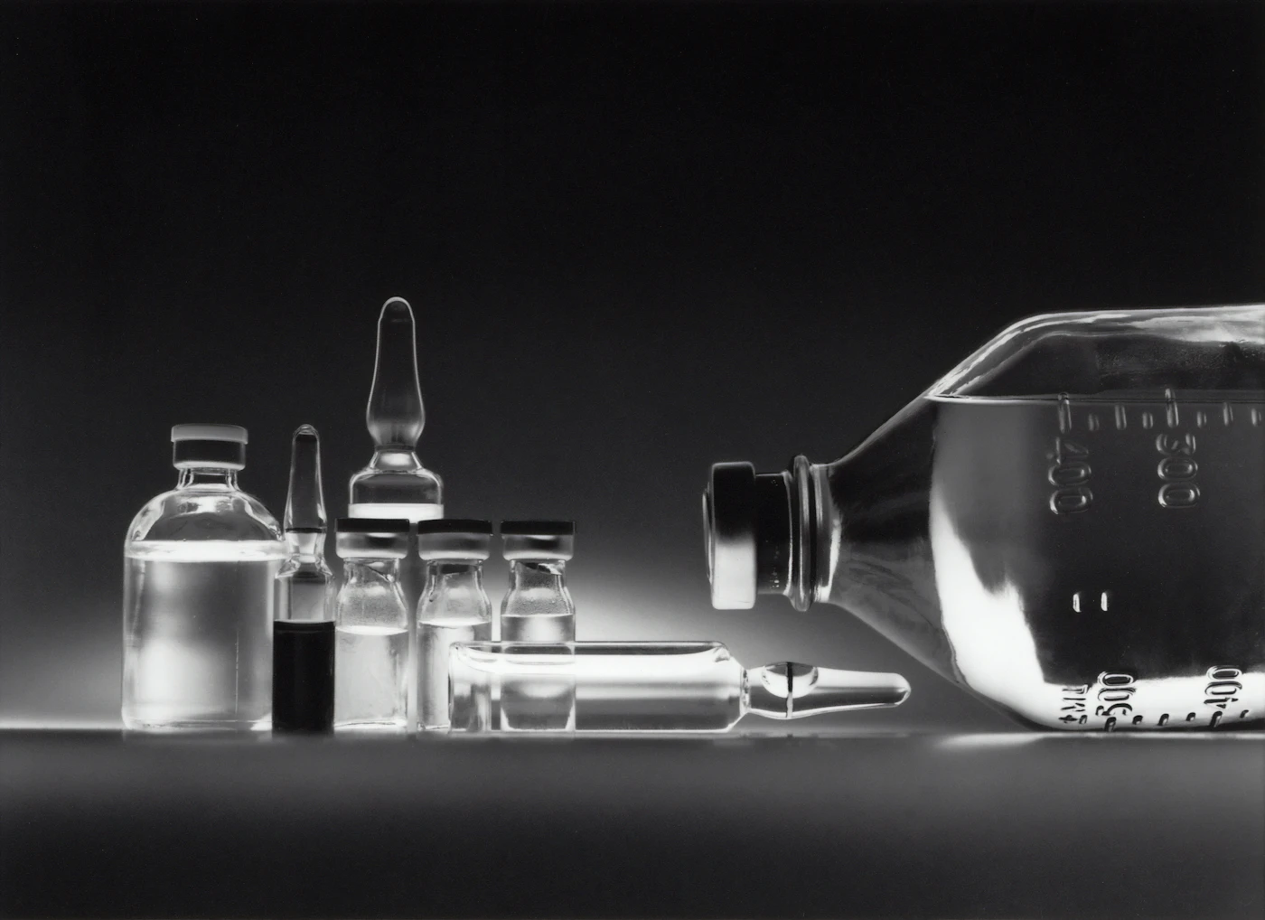 Glass medication vials and an IV fluid bottle on a dark surface