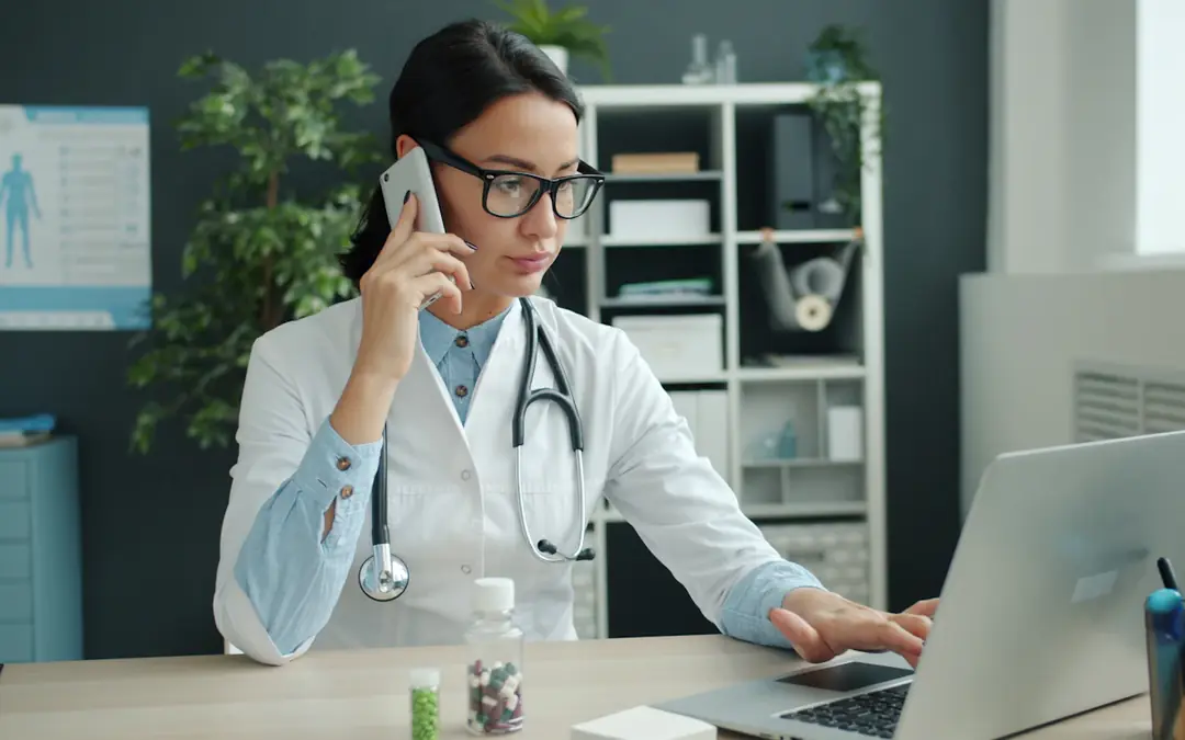 Physician on a phone call while working on a laptop