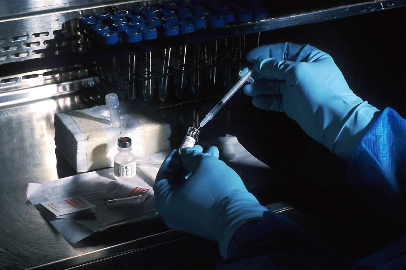 Gloved hands drawing medication from a vial into a syringe