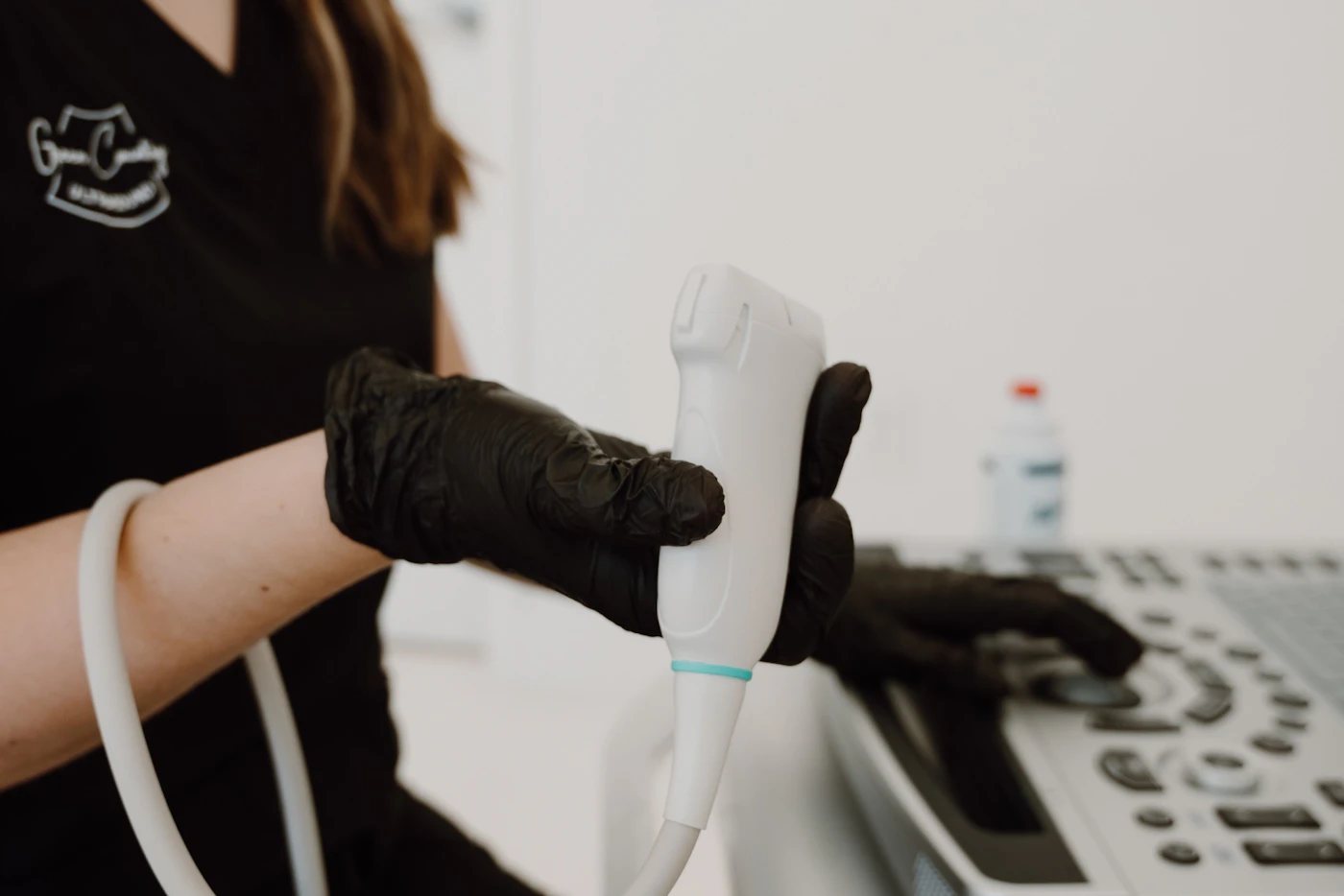 Gloved hand holding an ultrasound transducer next to the scanner console